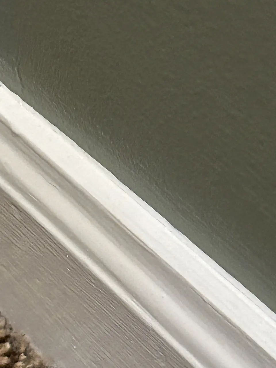 Close-up of freshly painted white baseboard against a green wall