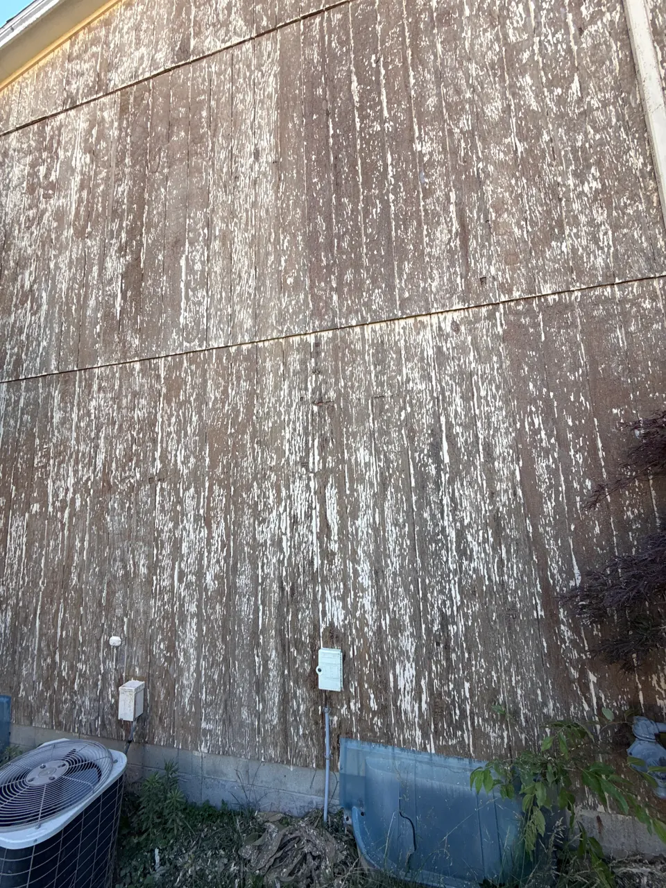 Wood siding with paint peeling down to bare, weathered wood