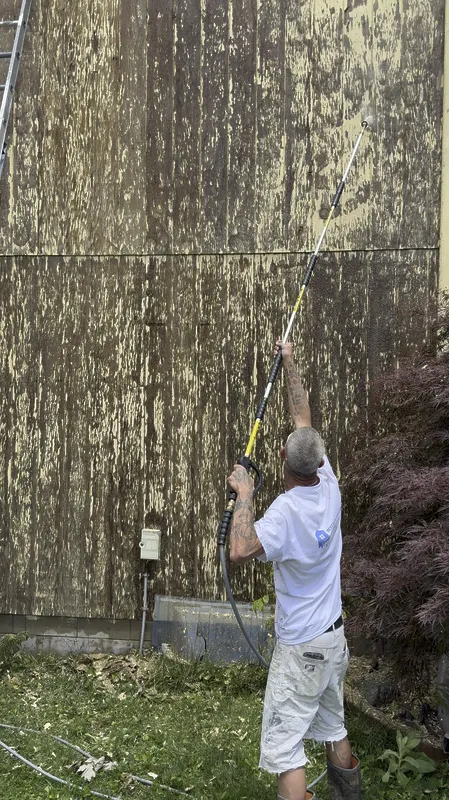 Crew member power washing wood siding before painting